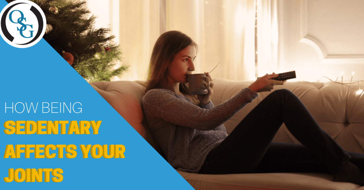 woman drinking a hot beverage out of a mug on the couch with a christmas tree watchng television clicking remote
