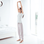 woman standing and stretching with arms raised above her head in bedroom