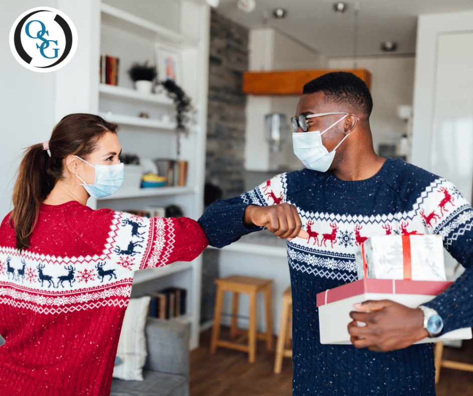 Two people wearing masks and holiday sweaters greeting each other by touching elbows