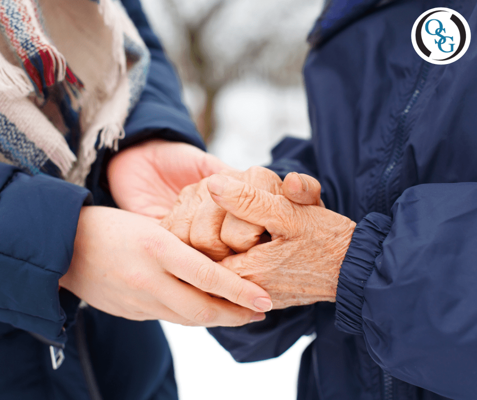 A close up of an elderly couples hands holding each other outside during winter