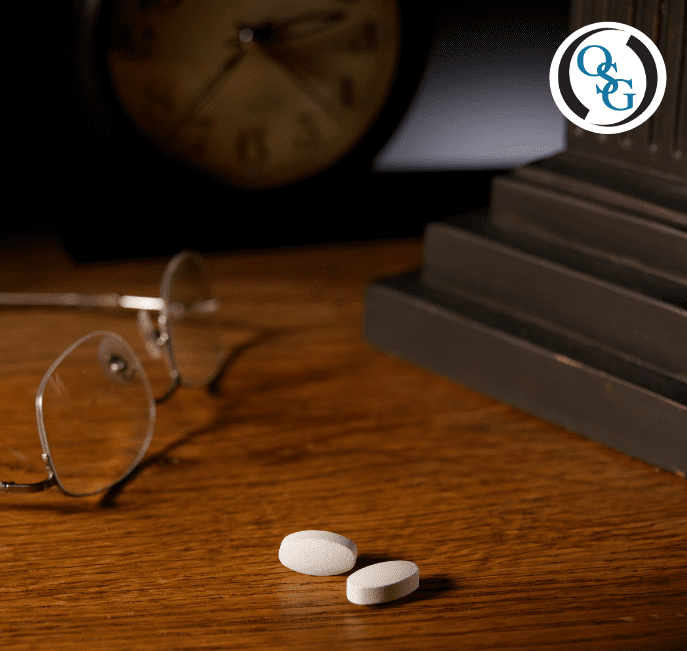Two pills and a pair of glasses sitting on a bedside table