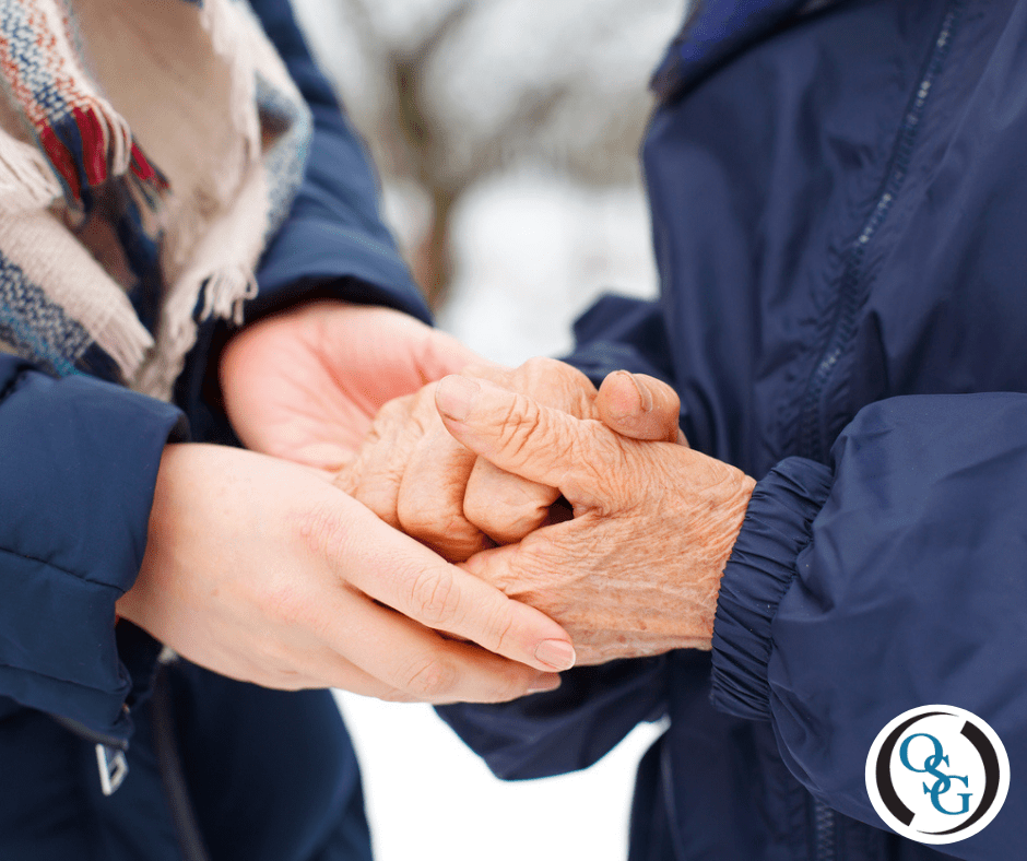 A woman holding her elderly mother's hands outside in the snow