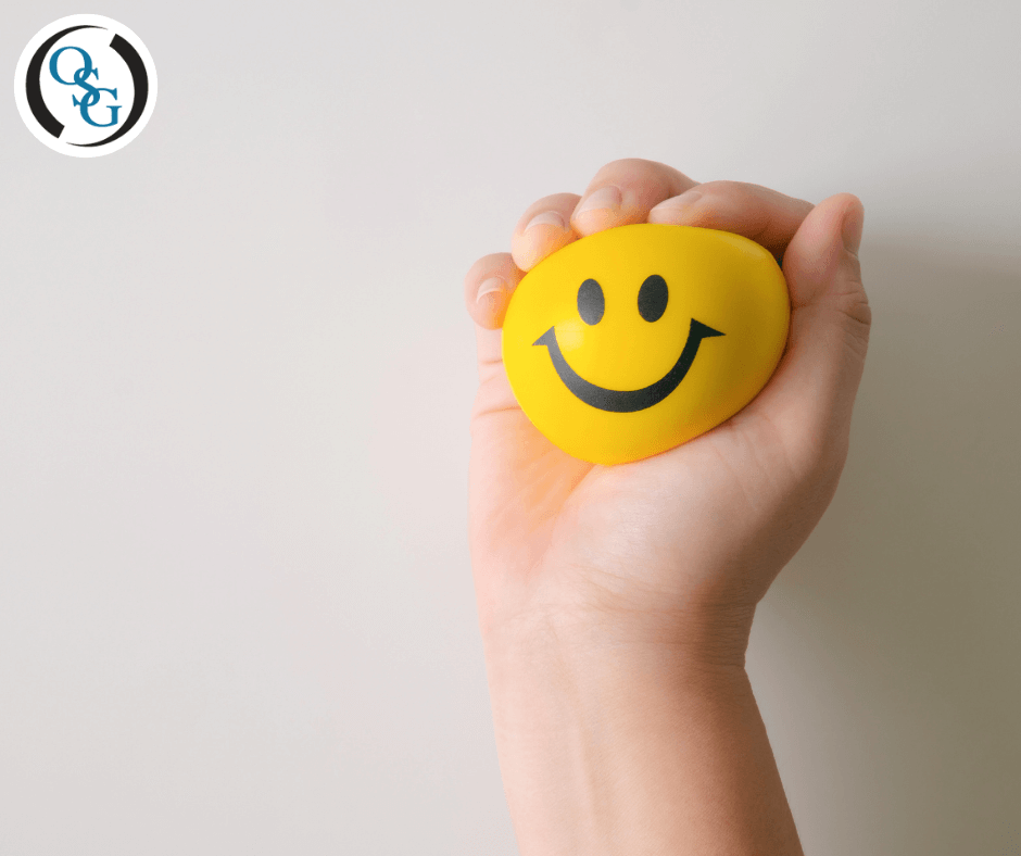 A hand holding a yellow, smiley face stress ball