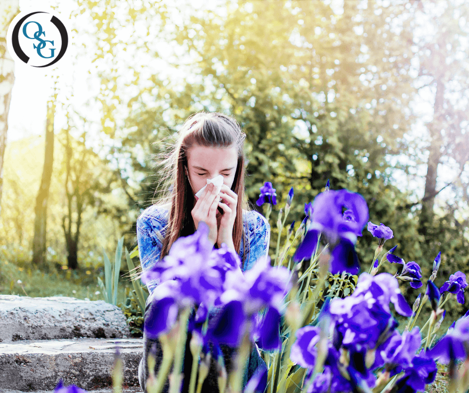 A woman sneezing into her tissues in front of spring flowers outdoors