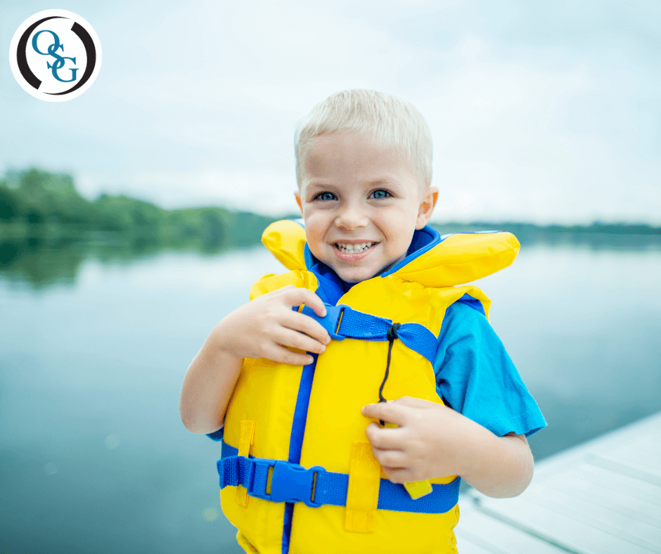 A young boy wearing a life jacket on a dock by a lake