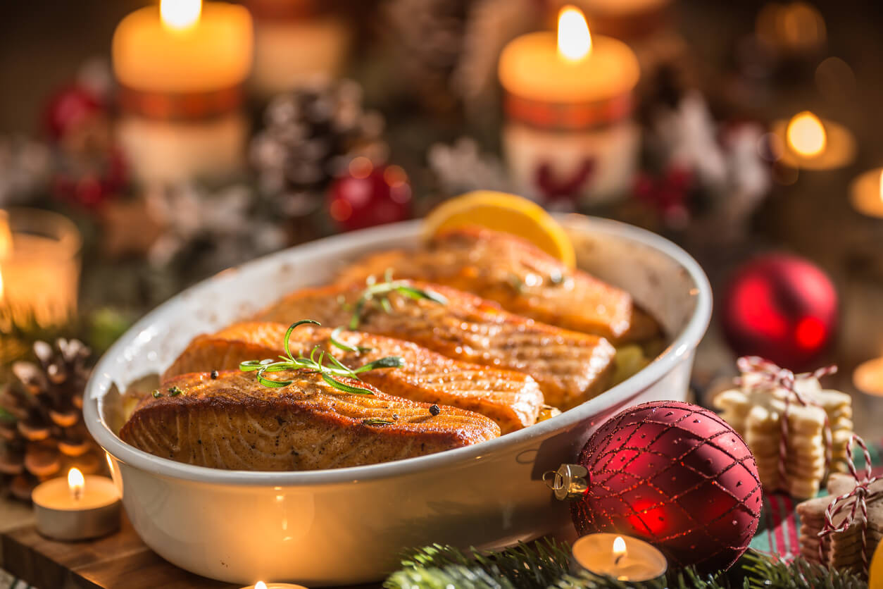 Christmas dinner from fish salmon in roasting dish with festive decoration advent wreath and burning candles .