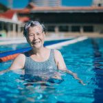 Asian chinese senior woman looking at camera smiling in swimming pool during weekend morning; benefits of swimming for joint health
