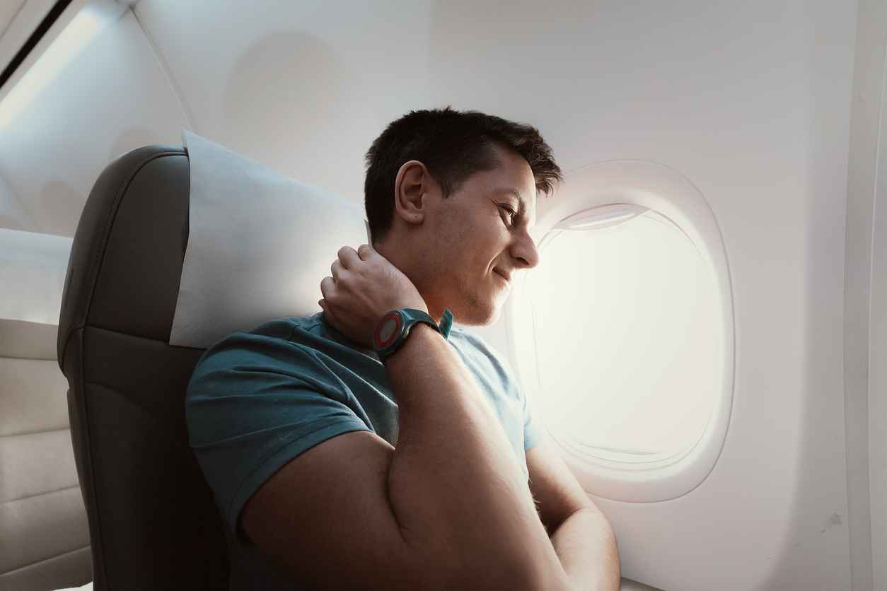 A man suffers from severe neck pain during a long flight in an uncomfortable position on an airplane. Joint pain travel tips
