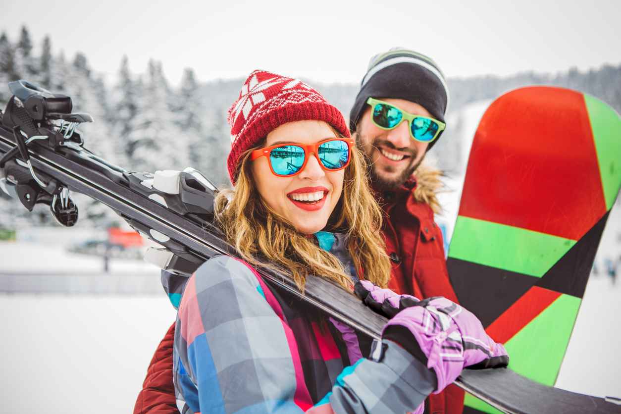 Couple on vinter vacation at mountain. Holding skis and preparing for skiing. Mountain is covered with snow.