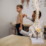 A pediatric neurologist doctor examines the back of a 5-year-old boy who has back pain. Treatment of muscle pain and scoliosis in children