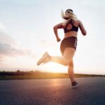 Sporty woman running at sunset on the road.