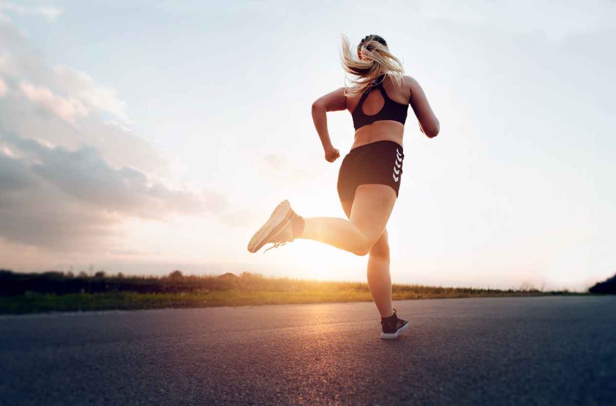 Sporty woman running at sunset on the road.