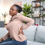Black woman suffering with back pain while sitting at home