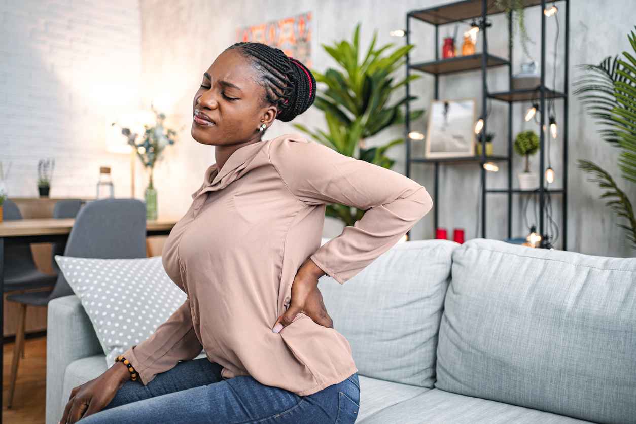 Black woman suffering with back pain while sitting at home