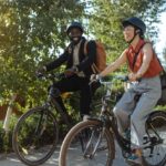 Two people enjoying a leisurely bike ride through a park setting. The sun shines brightly, casting a warm glow over the scene, and highlighting the joy of outdoor activities.
