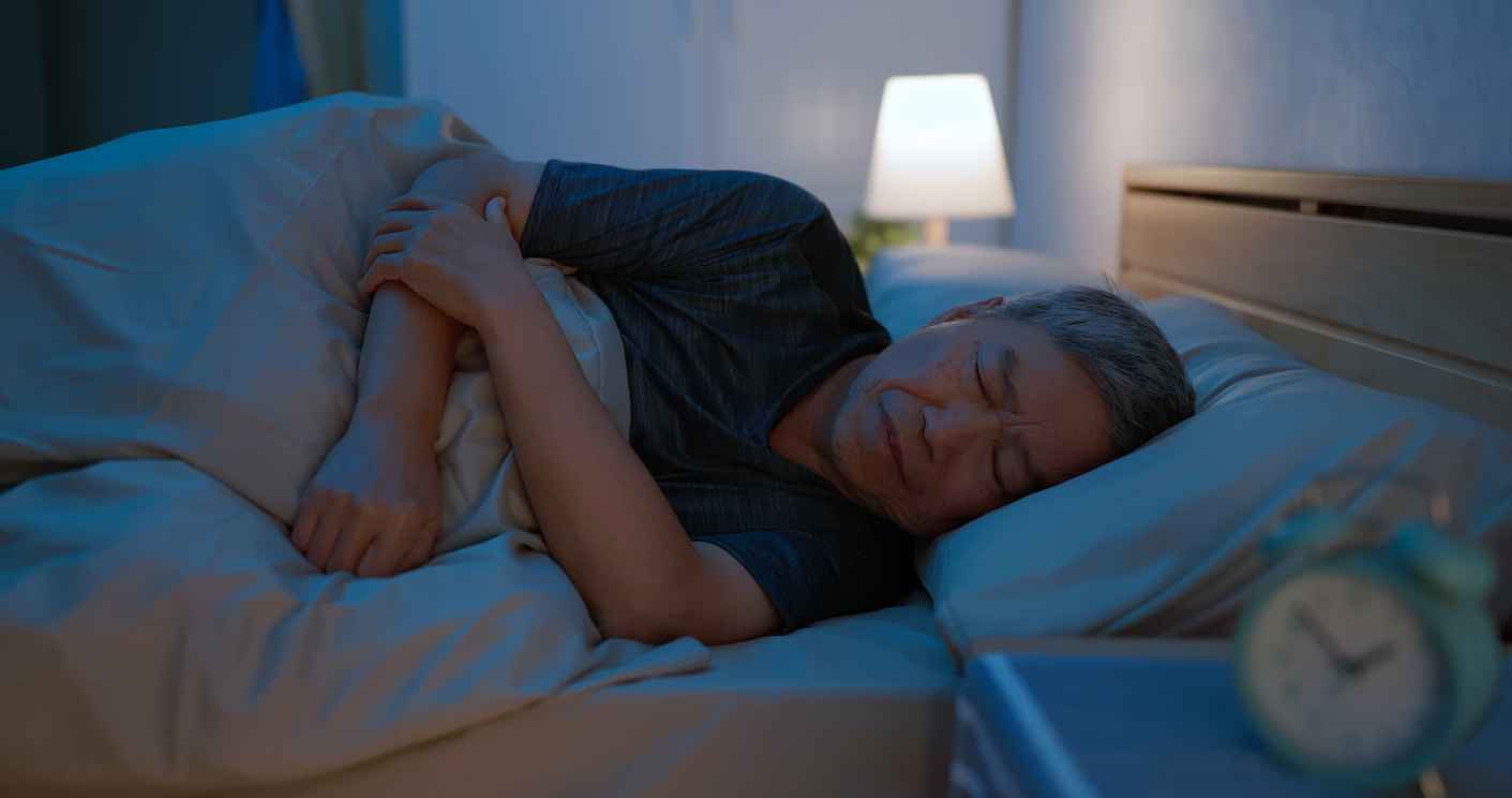 Asian old man laying on bed sleepless at night struggling with joint pain