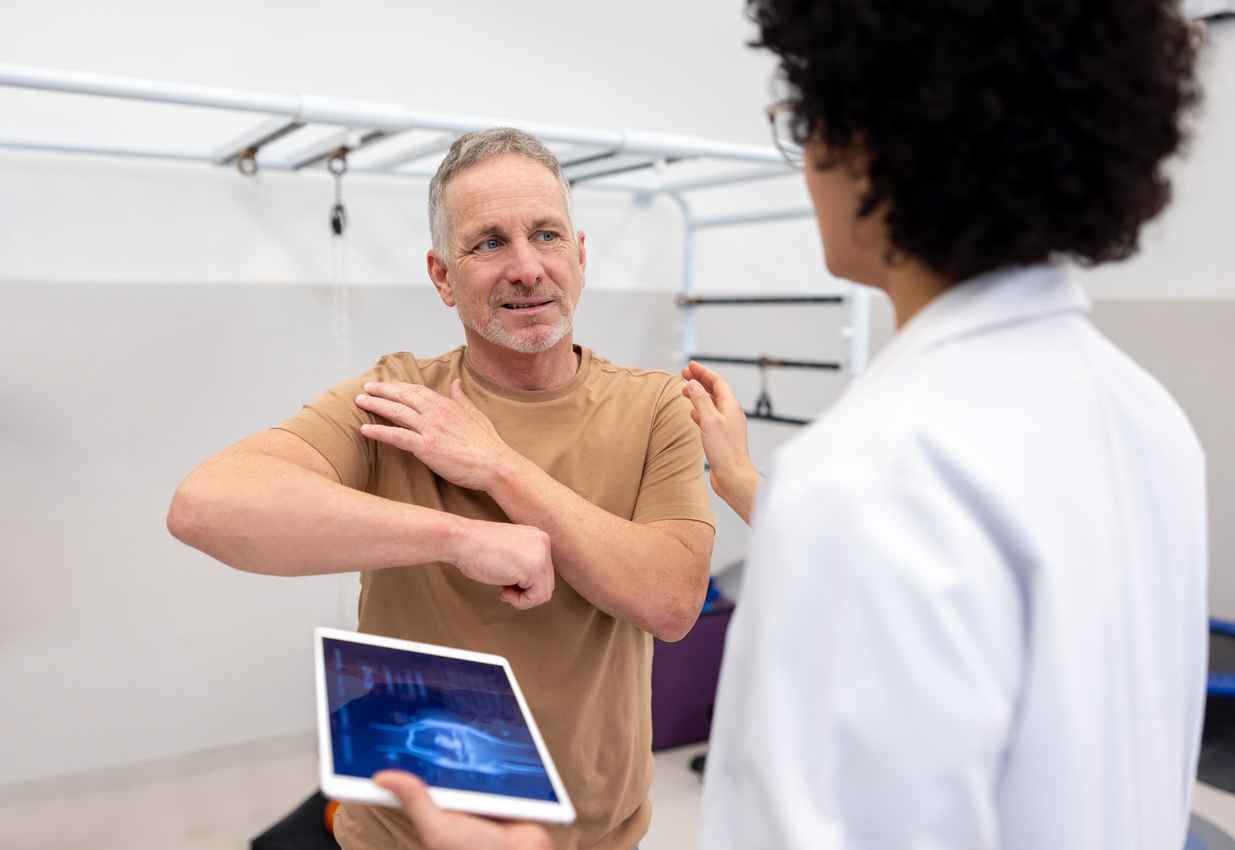 Mature Latin American patient talking to an orthopedist about pain in his shoulder