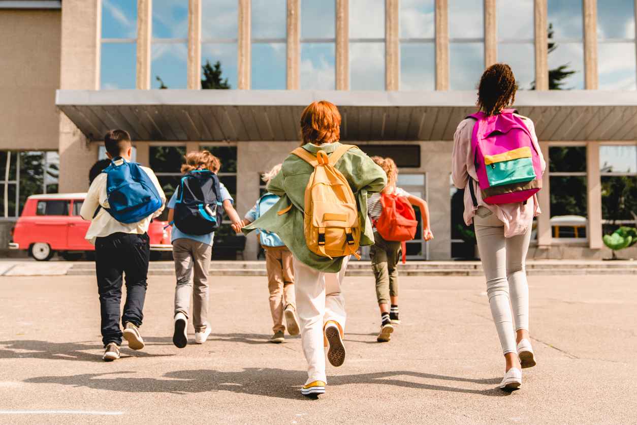 Little kids schoolchildren students running hurrying to the school building for classes lessons from to the school bus. Welcome back to school. The new academic semester year start