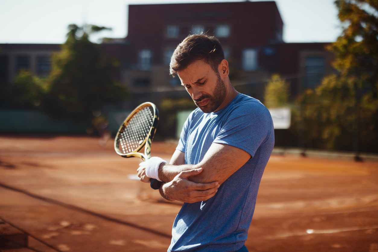 Sportsman clutching elbow in discomfort during tennis match. Ideal for illustrating overuse injuries, joint strain, and athletic health concepts.